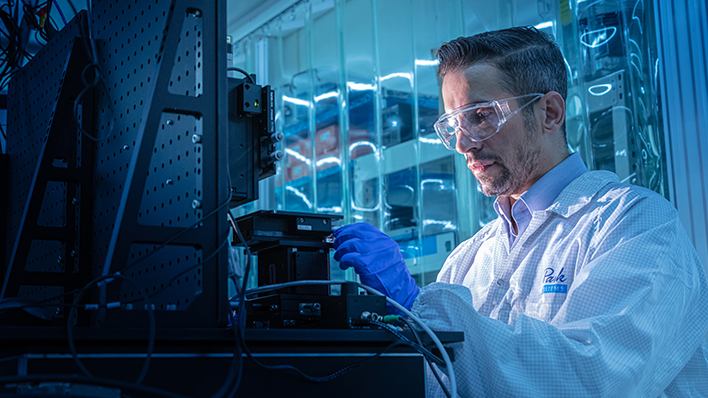 A man in a lab coat and goggles works on a piece of research equipment, highlighting the importance of active vibration isolation technology in ensuring reliable, high-resolution measurements in research.